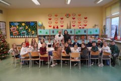 Grupa uczniów w strojach galowych siedząca przy stole świątecznie udekorowanym. 