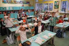 Grupa uczniów siedząca w ławkach, wykonująca pracę plastyczną pingwinka w czapce Mikołaja.