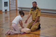 Dziewczynka klęcząca przed fantomem i wykonująca resuscytację.