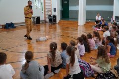 Grupa dzieci zgromadzona na sali gimnastycznej oraz strażak z fantomem człowieka.