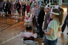 Dzieci, stanowiące widownię oraz członkowie koła teatralnego, mające na głowach opaski z wizerunkiem misia, pokazują gesty zgodnie ze słowami wymawianej rymowanki.