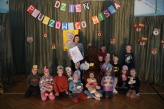 Pamiątkowe zdjęcia klas 1a, 1b, 1c, 1d, 1e, 1f z Pluszowym Misiem na tle dekoracji z napisem „Dzień Pluszowego Misia”.