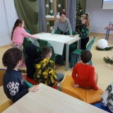 Dwie dziewczynki nakrywają obrusem świąteczny stół, w tle świąteczna dekoracja.