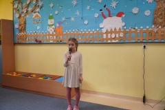 Dziewczynka śpiewa pastorałkę. W tle widać świąteczną dekorację.  