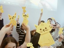 Grupa uczniów w bibliotece w wyciągniętych rękach prezentuje wykonane przez siebie żółte figurki origami – koty.