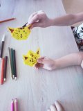 Dwoje uczniów – widać tylko ręce, w których trzymają niedokończone figury origami – głowy żółtych kotów.