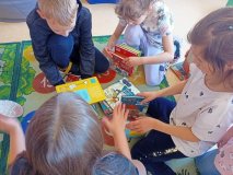 Grupa uczniów na podłodze w bibliotece próbuje z kilku książek wybudować wieżę.