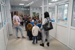 Grupa Dzieci przemieszcza się przez łącznik – szatnię do części, w której odbywają się zajęcia klas młodszych. Nauczyciel opowiada o miejscu, gdzie Dzieci rozbierają się.