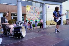 Na scenie nastolatek gra na gitarze a nastolatka gra na perkusji.