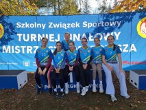 Na tle niebieskiego banneru z napisem Szkolny Związek Sportowy, Turniej Finałowy Mistrzostw Mazowsza stoi siedem dziewczynek w strojach reprezentacji szkoły.