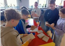 Grupa podekscytowanych uczniów ogląda przedmioty/książki zapakowane w szary papier.