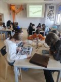 Pomieszczenie biblioteki, grupa uczniów siedzi przy stolikach skupiona na czytaniu, przeglądaniu książek, w tle na napis "Speed dating" - Szybka randka.