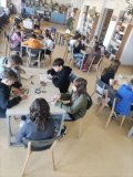 Pomieszczenie biblioteki, grupa uczniów siedzi przy stolikach skupiona na czytaniu, przeglądaniu książek.