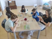 Pięcioro uczniów siedzi w bibliotece przy stolikach, są skupieni na czytaniu, przeglądaniu książek.