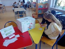 Dwie uczennice siedzą przy stoliku wyraźnie zajęte pisaniem na kartce - obok pudło z napisem Wybory Książek.