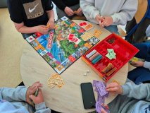 grupa Uczniów przy okrągłym stoliku gra w planszówkę „Monopoly Płock”
