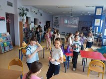 pomieszczenie biblioteki w trakcie wydarzenia „Hogwartowy challenge”, na zdjęciu duża grupa dzieci zaangażowana w różne aktywności, między innymi skupiona wokół koła fortuny, które było tzw. Tiarą Przydziału
