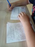 Uczeń siedzi przy stole w czytelni, widać tylko dłonie, rozwiązuje test wiedzy o zaklęciach
