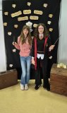 Dwie Uczennice pozują do zdjęcia na tle czarnej ścianki z napisem „Ogólnopolski Tydzień Bibliotek”, „Hogwartowy challenge”, są w stroju Hermiony, jedna w oficjalnym szkolnym stroju, druga w stroju codziennym, obie w dłoniach mają różdżki