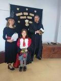 kobieta i mężczyzna – bibliotekarze w strojach czarodziejów wręczają nagrodę i gratulują Uczennicy, która brała udział w konkursie na najciekawsze przebranie w stylu bohaterów książek o Harrym Potterze, Uczennica jest w przebraniu Hermiony