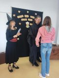 kobieta i mężczyzna – bibliotekarze w strojach czarodziejów wręczają nagrodę i gratulują Uczennicy, która brała udział w konkursie na najciekawsze przebranie w stylu bohaterów książek o Harrym Potterze, uczennica jest przebrana za Hermionę