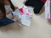 Dwie dziewczynki na podłodze, biorą udział w segregowaniu kolorowych karteczek z akcji walentynkowej organizowanej przez samorząd.
