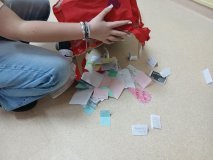 Osoba siedząca na podłodze, wysypuje z czerwonego pudełka różnorodne karteczki uzbierane w ramach akcji walentynkowej samorządu uczniowskiego. 