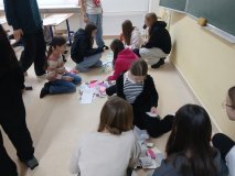 Młodzież w sali lekcyjnej siedząca na podłodze, zajęta segregowaniem różnorodnych, kolorowych karteczek na walentynki. 