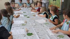 Uczniowie przygotowani do wykonania prac siedzą w fartuchach przy stole.