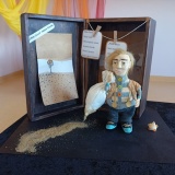 Miniaturowa scenografia do wiersza Juliana Tuwima „Idzie Grześ przez wieś”. Na tle czarnej drewnianej skrzynki widać postać człowieka. W worku na plecach niesie piasek, który przez dziurkę wysypuje się za nim.