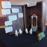 Miniaturowa scenografia do książek Tove Jansson z serii „Muminki”. Na tle brązowej skrzynki widać figurki Muminków, obok zielonego namiotu Włóczykija, a na podeście Małą Mi oraz Ryjka.