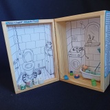 Miniaturowa scenografia do wiersza Aleksandra Fredry „Małpa w kąpieli”. W skrzyneczce znajdują się biało-czarne ilustracje do wiersza – wnętrze łazienki oraz miniaturowa figurka małpy kąpiącej się w wannie.