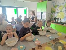 Uczniowie łączą w misce wszystkie produkty potrzebne do upieczenia ciasteczek owsianych. Na zdjęciu widoczne są trzy dziewczynki i jeden chłopiec, którzy wspólnie pracują nad przygotowaniem masy owsianej