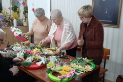 Seniorzy wykonują stroiki z materiałów dekoracyjnych.