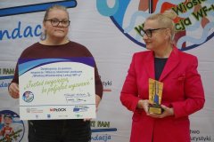 Stojąc przed banerem Pani Wicedyrektor Monika Przemyłska trzyma duży dyplom, a Pani Dyrektor Szkoły Marlena Błachowicz trzyma sportowe trofeum.