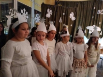 Na tle dekoracji widać ustawione w rzędzie dziewczynki, odgrywające role Śnieżynek, ubrane w białe stroje z białymi opaskami na głowach.