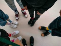 Na tle jasnej podłogi ustawionych w okrąg jest sześcioro osób, które pokazują swoje kolorowe skarpetki, często nie do pary.