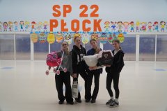 W przestronnej sali z dużym, pomarańczowym napisem "SP 22 Płock" oraz kolorowymi postaciami dzieci oraz dużymi wielobarwnymi pisankami z kartonu w tle cztrey uczennice klas 4-8 ze wsoimi zamiennikami plecaków (wózek dla lalek, duża latarenka, powłoczka na poduchę i transporter zwierzęcy