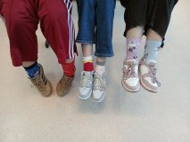 Na tle jasnej podłogi widać trzy pary nóg uczniów, którzy demonstrują swoje kolorowe skarpetki.