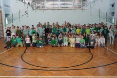 Na sali sportowej bardzo duża grupa uczniów klas 1-3 w różnorodnych zielonych ubraniach, wszyscy uśmiechnięci i radośni.