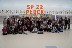W przestronnej sali z dużym, pomarańczowym napisem "SP 22 Płock" oraz kolorowymi postaciami dzieci oraz dużymi wielobarwnymi pisankami z kartonu w tle duża ilość uczniów klas 4-8 oraz nauczycieli, każdy z wymyślną, szaloną fryzurą. Wszyscy w doborowym nastroju.