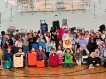 Na sali gimnastycznej część dużej grupy uczniów klas 1-3 w wymyślnymi zamiennikami plecaków w rękach (np. walizki, kuferki, kosze, tranporter zwierzęcy, oraganizery, worki itp.). Wszyscy z zadowolonymi minami.