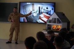 Mężczyzna w mundurze strażackim omawia prezentowany na ekranie film. 