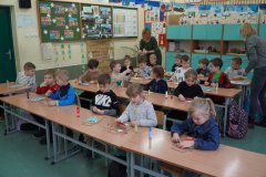 Przedszkolaki pracujące przy stolikach pod opieką nauczycieli.