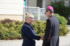 Zdjęcie przedstawia p. dyrektor Marlenę Błachowicz witającą się z Księdzem Biskupem Mirosławem Milewskim przed budynkiem szkoły