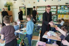 Ksiądz Biskup rozdaje dzieciom pamiątkowe obrazki, w tle widzimy trzech księży.
