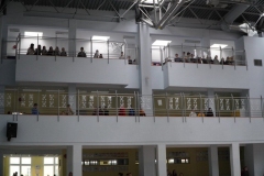 Uczniowie klas IV-VIII, stojący na rożnych poziomach budynku, obserwują wyświetlaną na forum szkoły prezentację multimedialną.