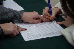 Zbliżenie na dłonie nauczycielki uczestnhiczącej w komisji wyborczej oraz uczennicy podpisującej się na liście wyborców podczas szkolnych wyborów do Młodzieżowej Rady Miasta Płocka.