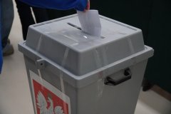 Zbliżenie na moment wrzucania karty do głosowania do urny wyborczej oznaczonej godłem Polski podczas szkolnych wyborów do Młodzieżowej Rady Miasta Płocka.