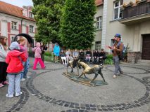 Przewodnik opowiada uczniom o historii Starego Rynku. Dzieci stoją w półkolu, słuchają z zaciekawieniem.